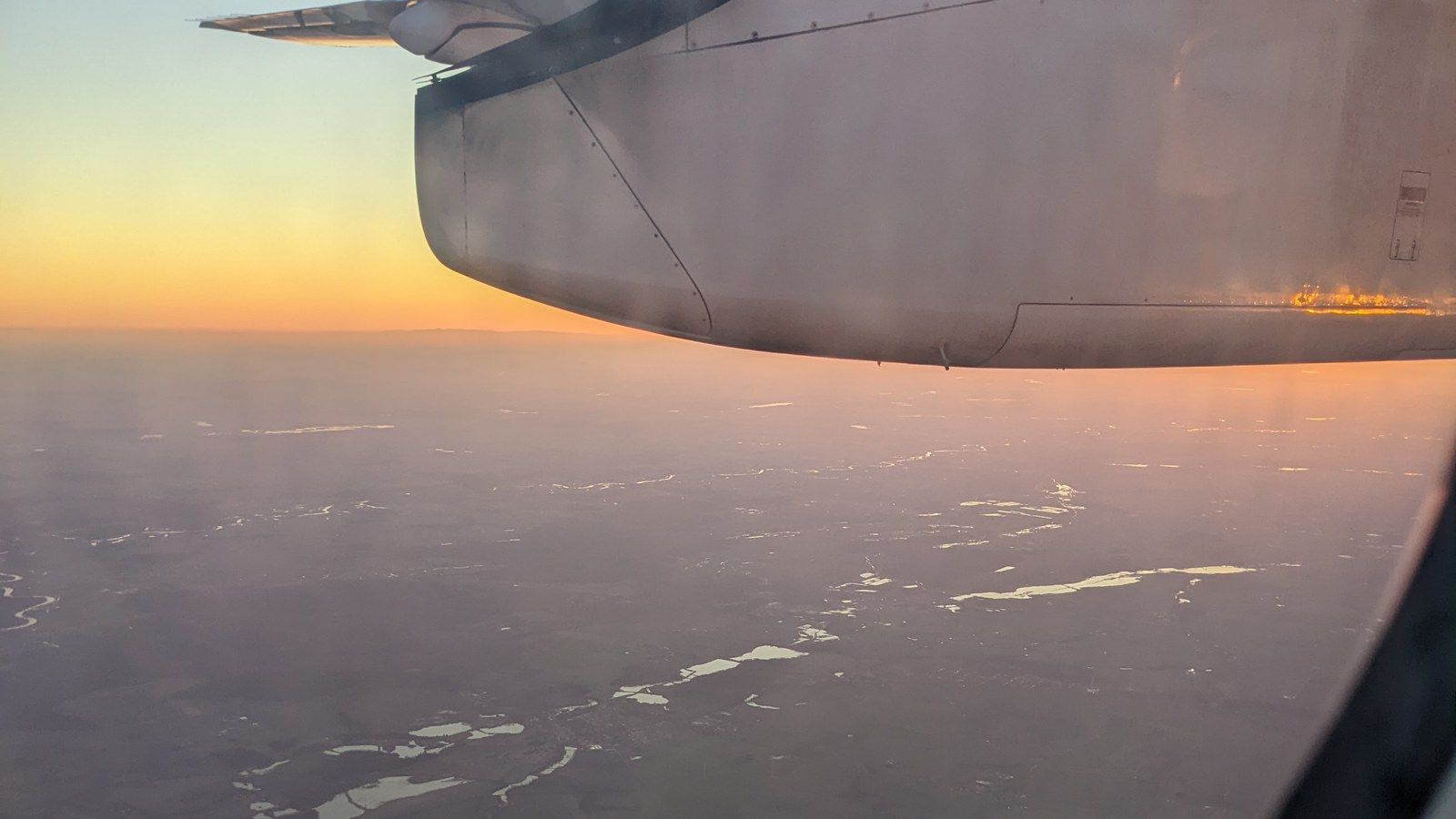An airplane wing over a city at sunset, photographed on 13 February 2022
